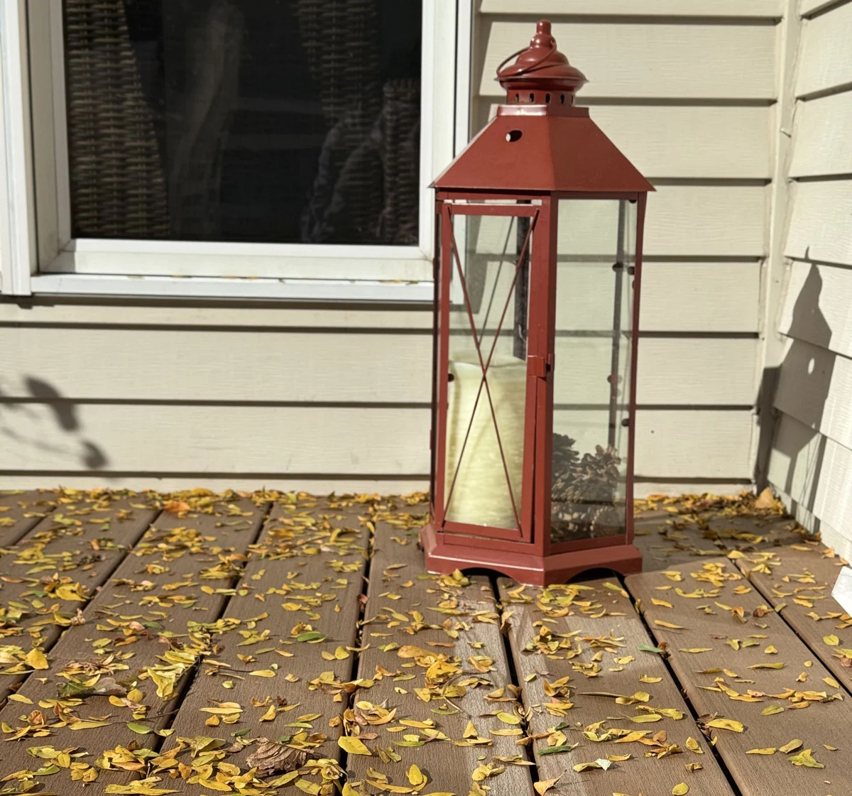 Red Lantern On A Composite Deck Covered In Fallen Autumn Leaves