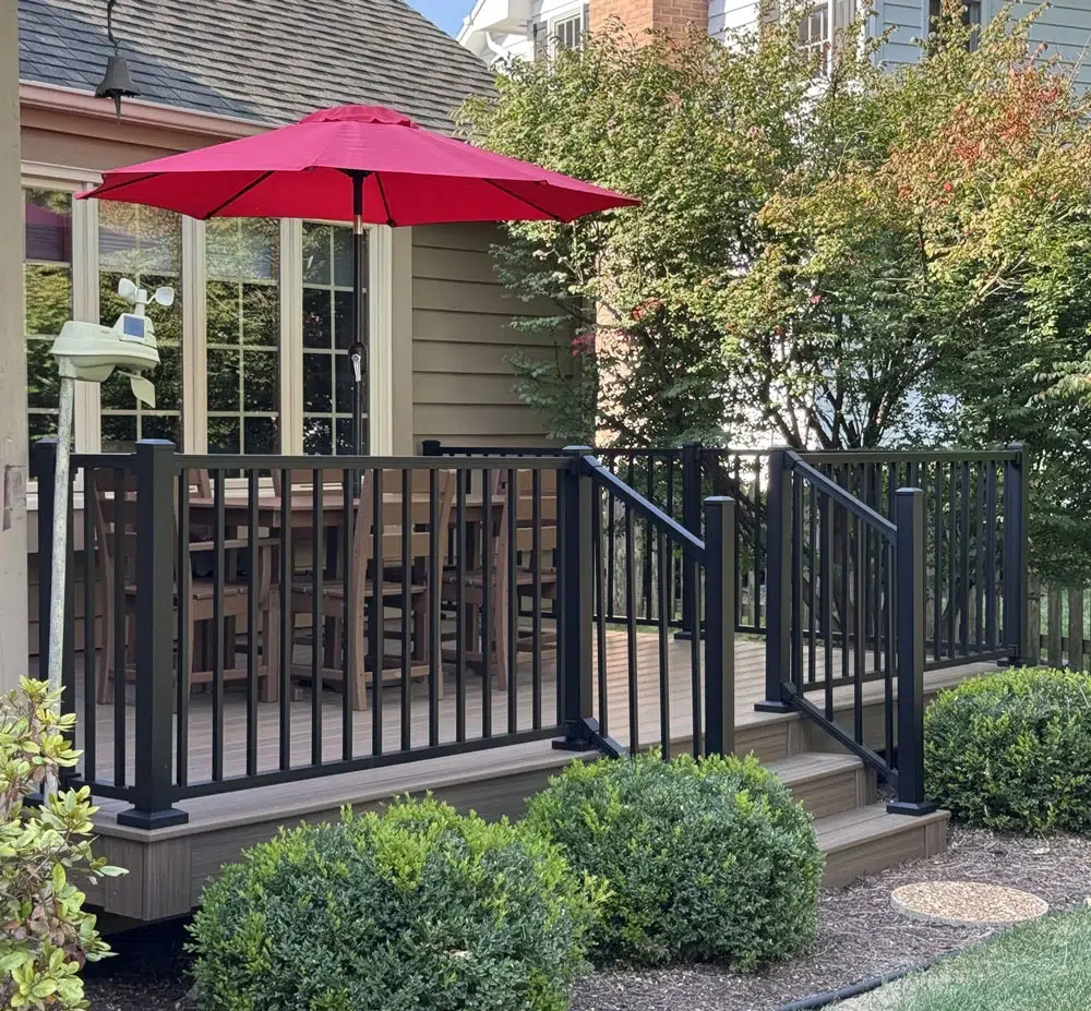 Completed Composite Deck With Black Aluminum Railing And Stair Access Surrounded By Landscaped Yard Built By Royal Deck Builders