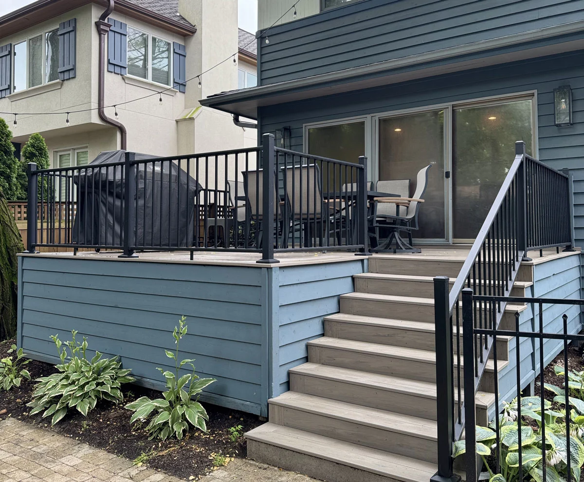Elevated composite deck with black aluminum railings and wide stairs attached to a two-story home Elevated Composite Deck With Black Aluminum Railings And Wide Stairs Attached To A Two-Story Home