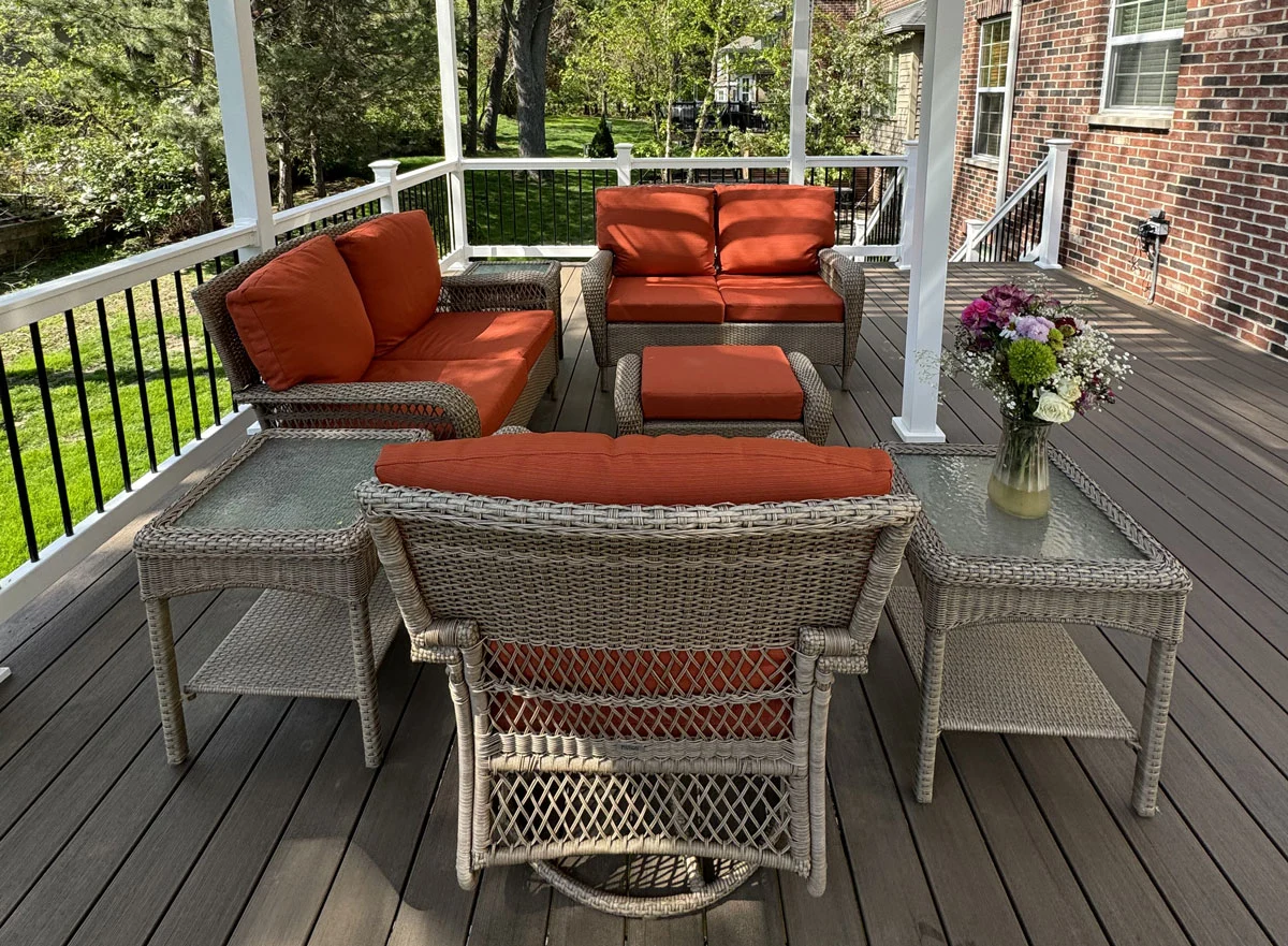 Wicker Patio Furniture With Orange Cushions Arranged On A Covered Composite Deck
